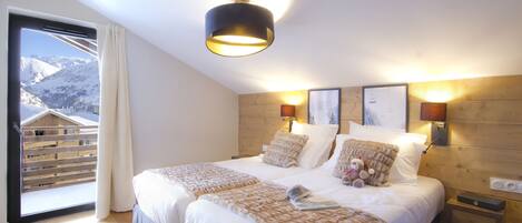 Une chambre avec deux lits, une grande fenêtre donnant sur les montagnes, une tête de lit en bois et des lampes fixées au mur.