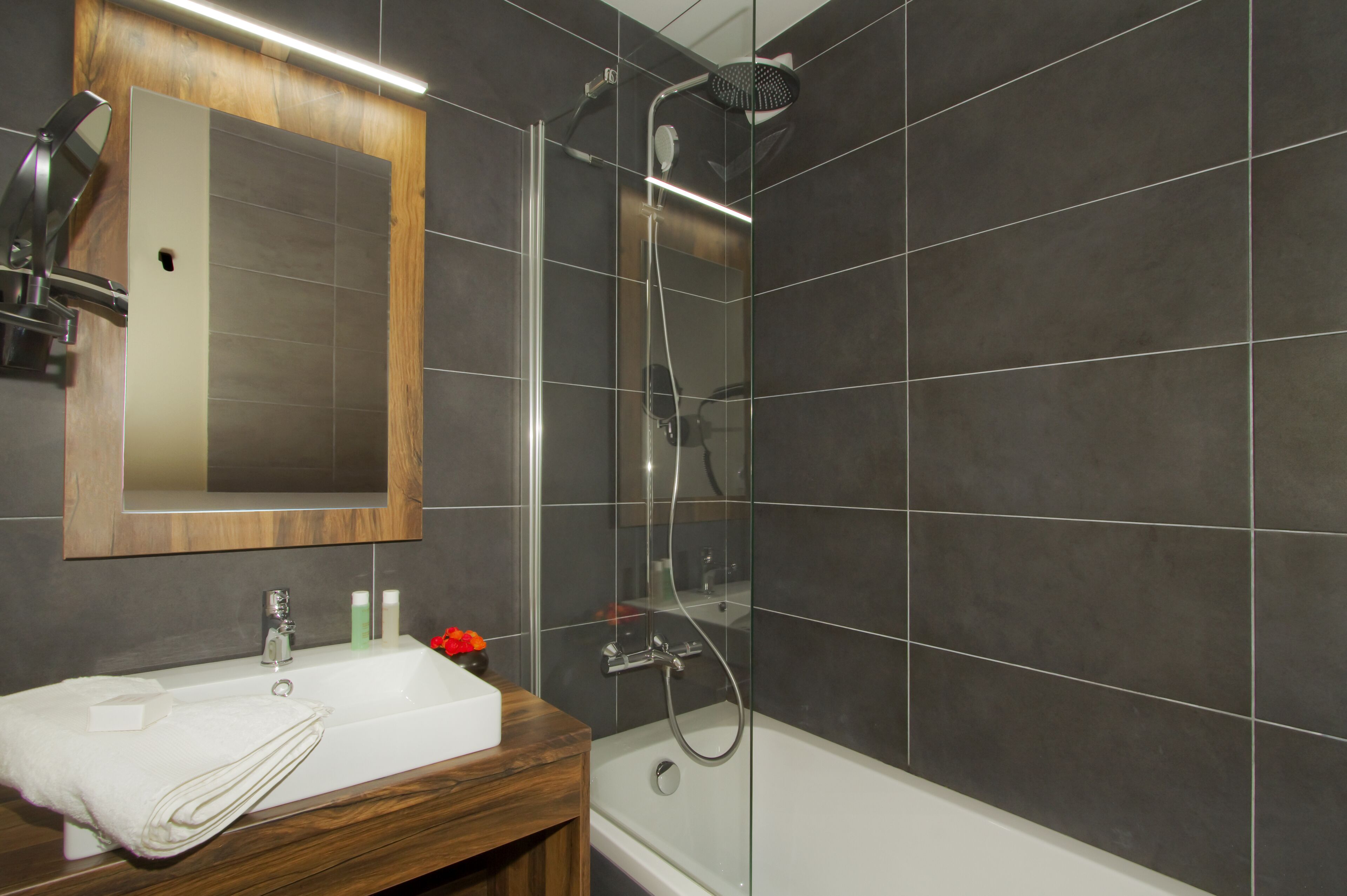 Une salle de bain avec un meuble-lavabo en bois, un miroir, un lavabo blanc et une douche à parois de verre.