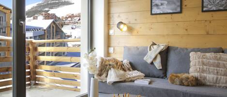 A cozy room with a wooden floor, a grey sofa, a chessboard, and a view of a snowy mountain.