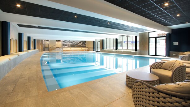 En swimmingpool med flisegulv, liggestole og udsigt til et bjerge landskab.