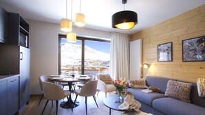 En moderne stue med sofa, spisebord og stole. Der er udsigt til bjerge gennem et stort vindue.