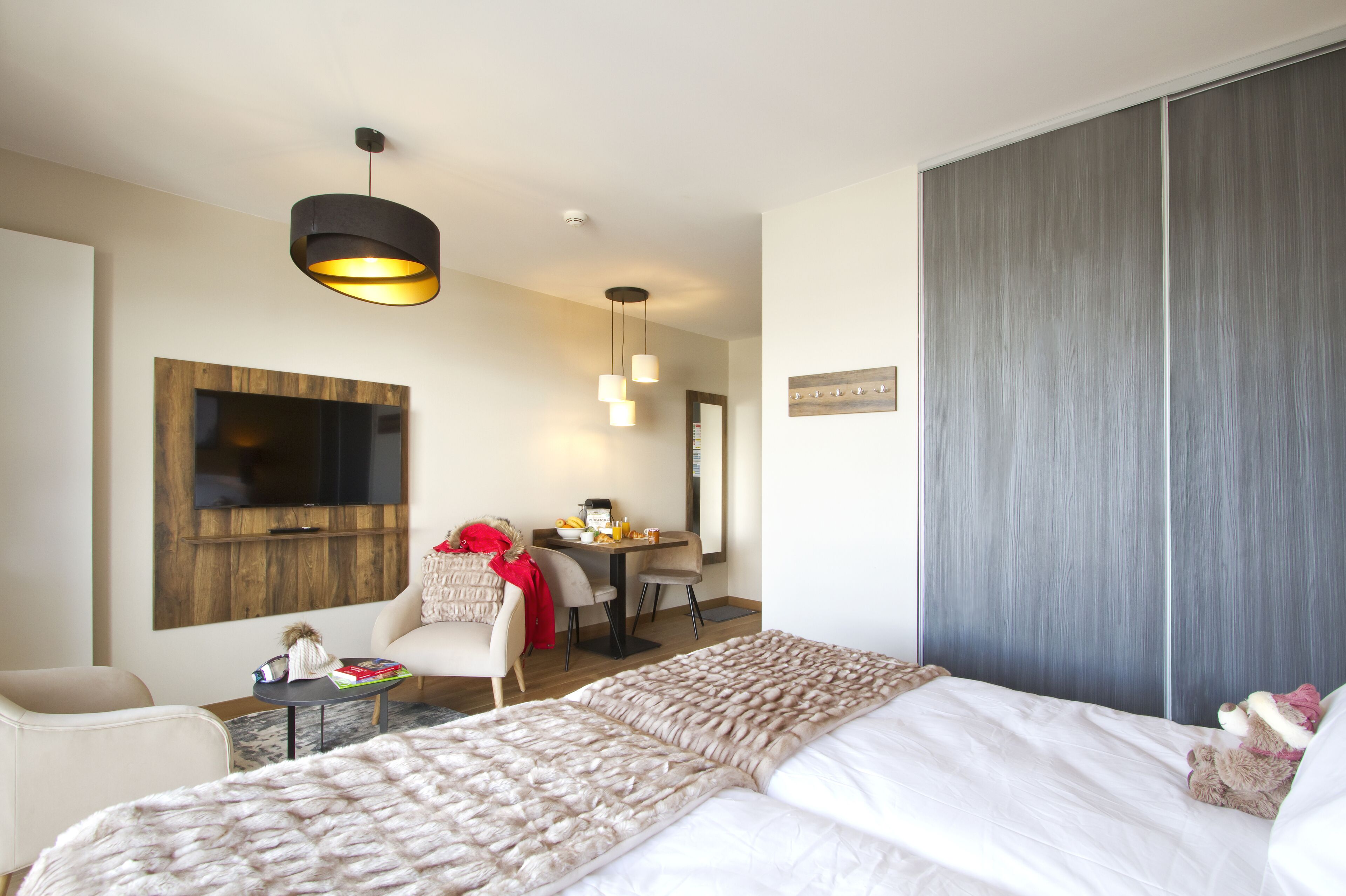 Una habitación de hotel moderna con una cama grande, un escritorio con silla, un televisor montado en la pared y un armario.