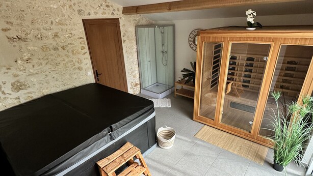 Een kamer met een zwarte bank, een houten kruk, een glazen douchecabine, een houten kast met glazen deuren en een stenen muur.