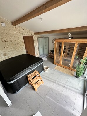 Una habitación con un sofá negro, un taburete de madera, una cabina de ducha de cristal, un mueble de madera con puertas de vidrio y una pared de piedra.