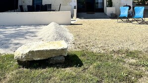 Een gebouw met twee verdiepingen, voorzien van een pannendak, een balkon en een voordeur. Twee blauwe stoelen staan buiten en op de voorgrond ligt een grote rots.