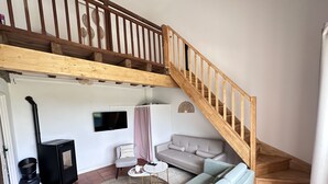 Een woonkamer met een bank, een televisie, een open haard en een houten trap.