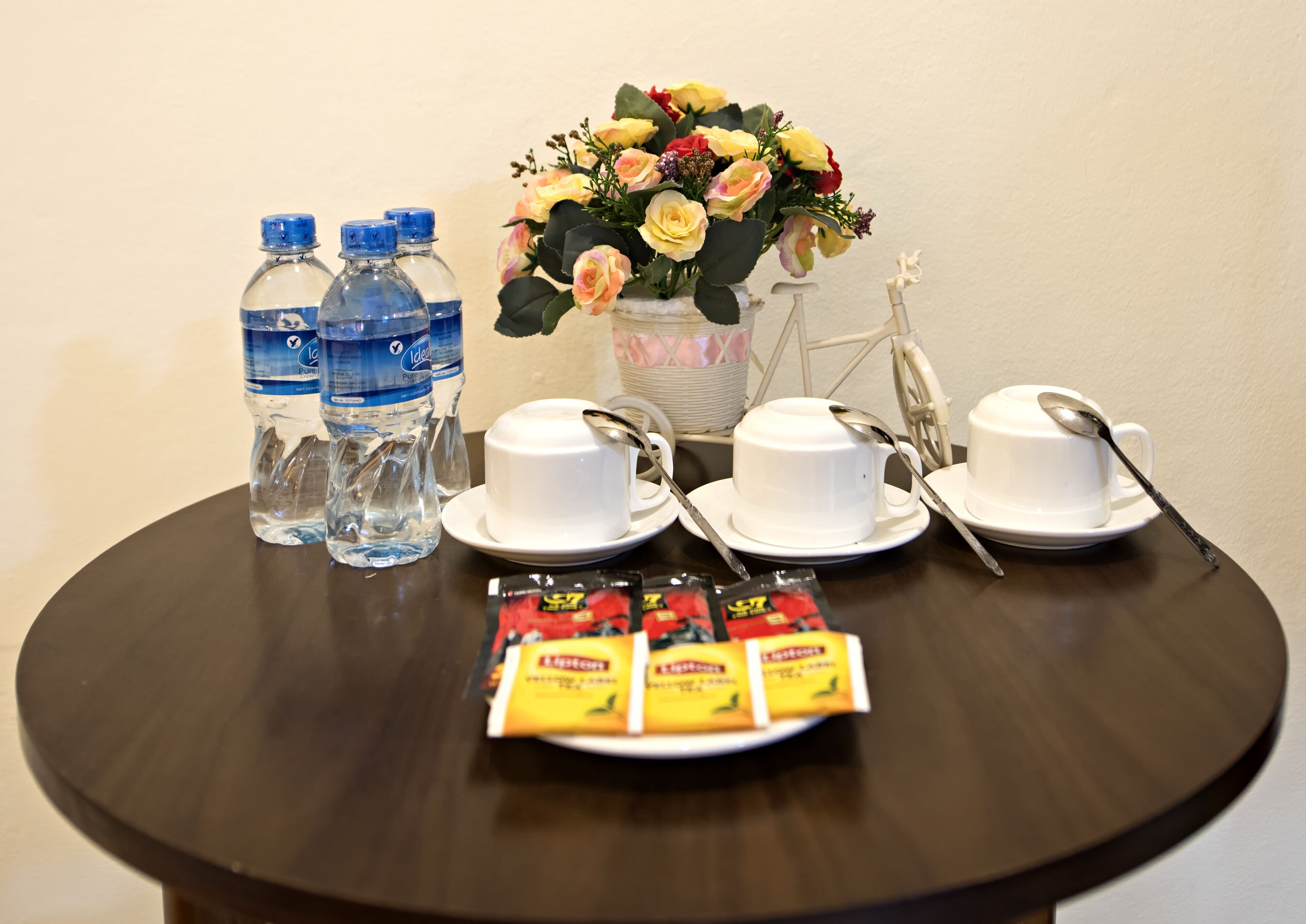 Una mesa con botellas de agua, vasos, cucharas y sobres de café instantáneo.