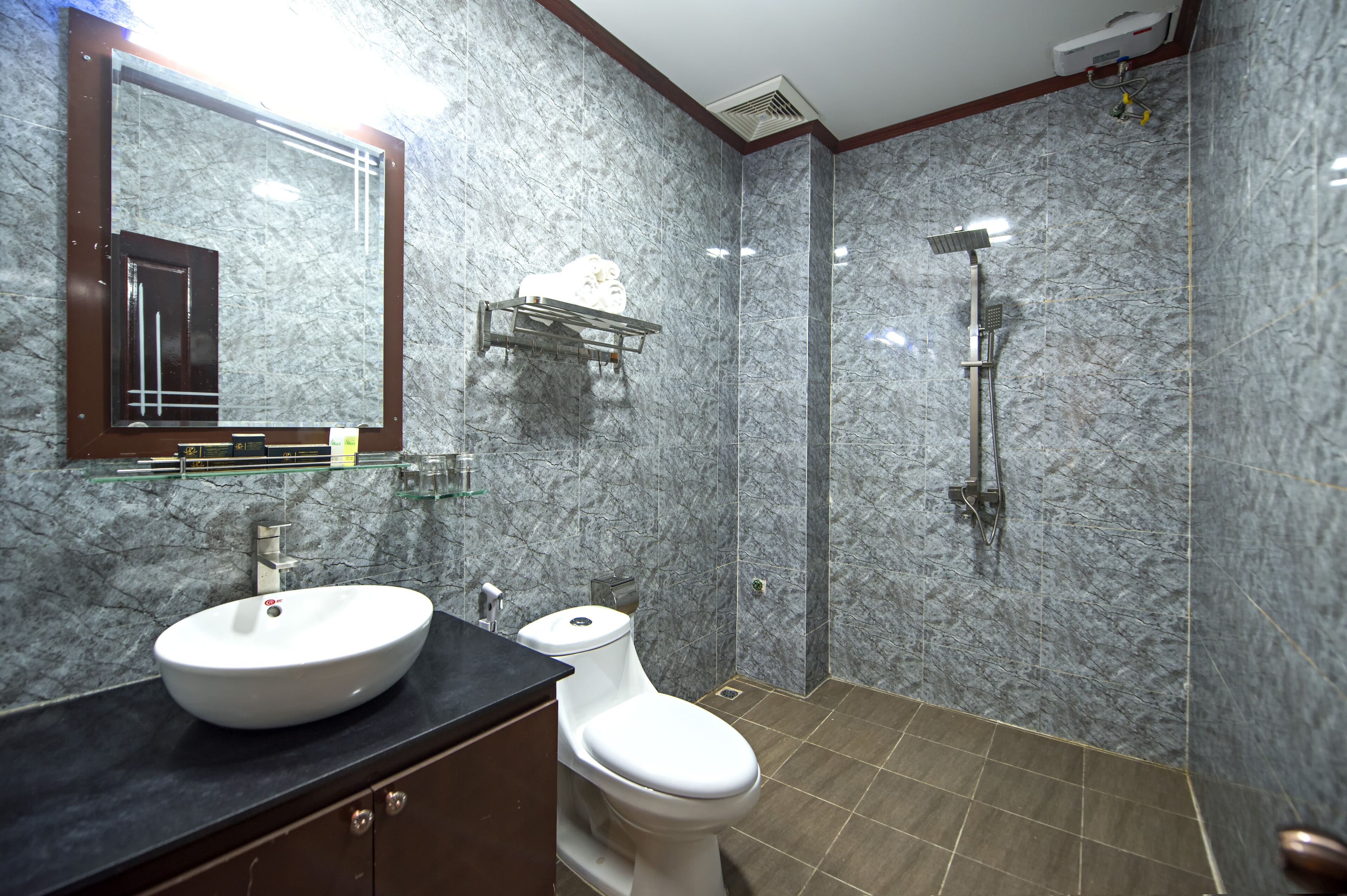 Un baño con pared de mármol, lavamanos blanco, inodoro y ducha.