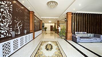 Un lobby espacioso con piso de mármol, una pared decorativa, un sofá y una araña.