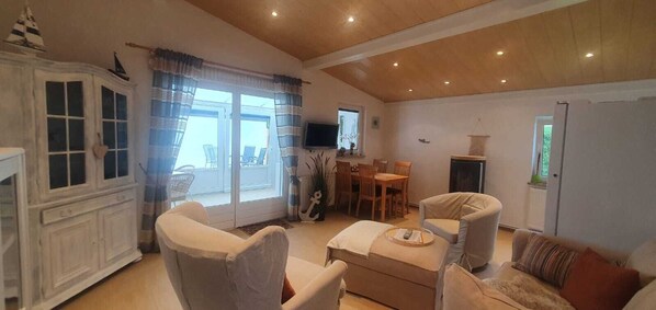 Amplia sala de estar con techo de madera, comedor con mesa y sillas, y un ventanal con cortinas.