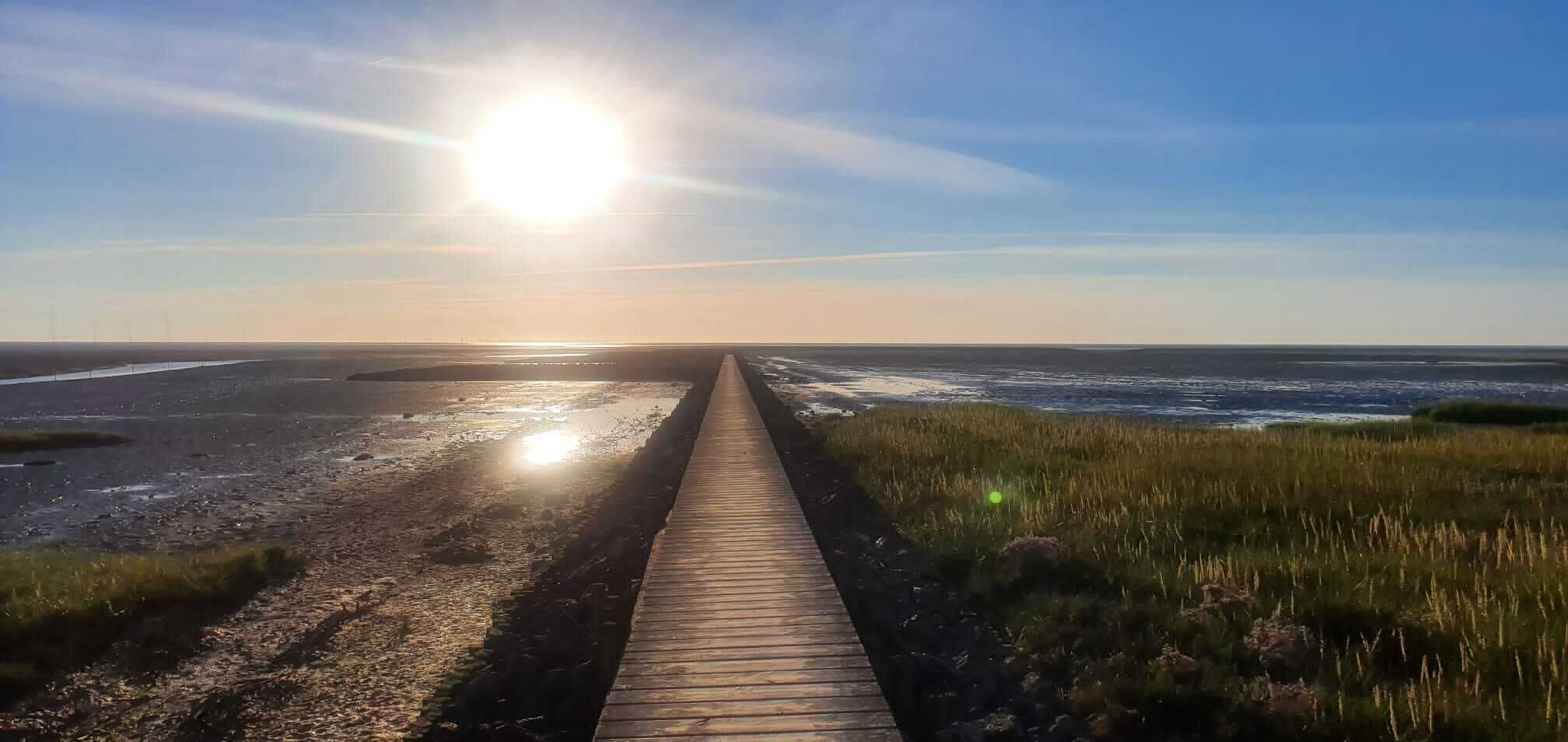 Una pasarela de madera que conduce a una playa con el sol bajo en el horizonte.