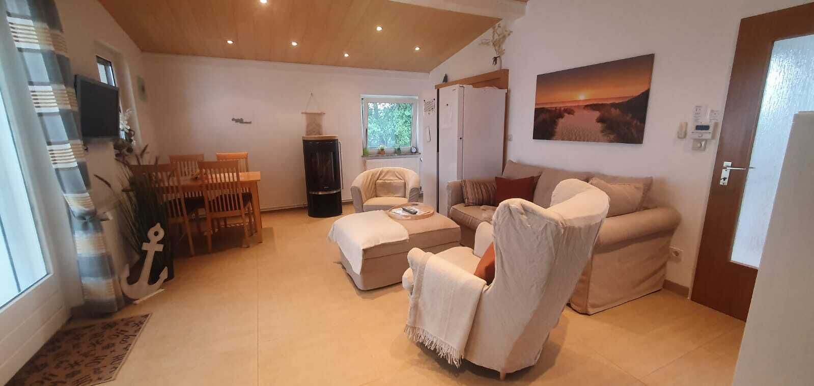 Un salon spacieux avec un canapé, un fauteuil et une table à manger. Un téléviseur est fixé au mur, et un tableau est visible.