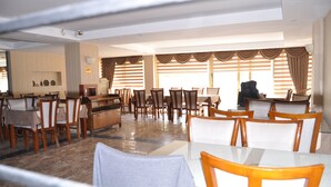 A spacious dining area with multiple tables and chairs, a fireplace, and large windows with curtains. - Arikan Otel (Pozanti)