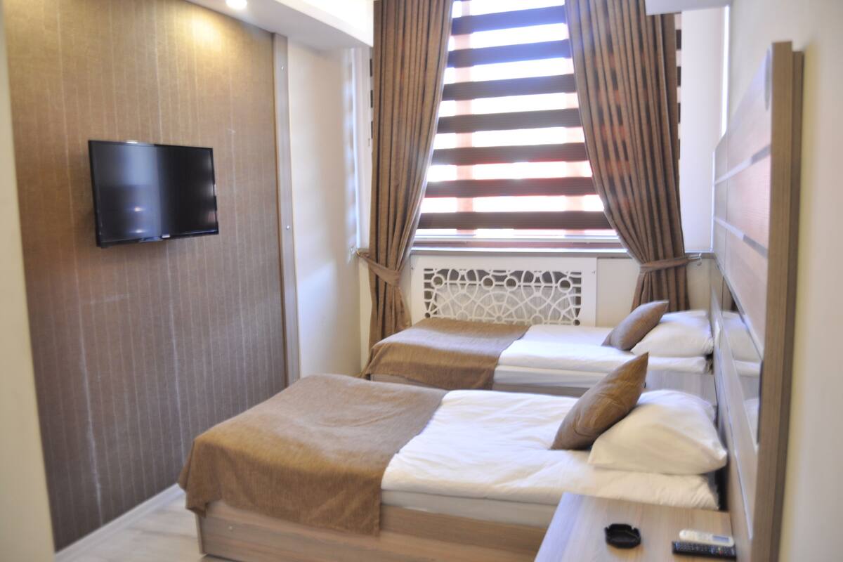 A hotel room with two beds, a TV mounted on the wall, and a window with curtains.