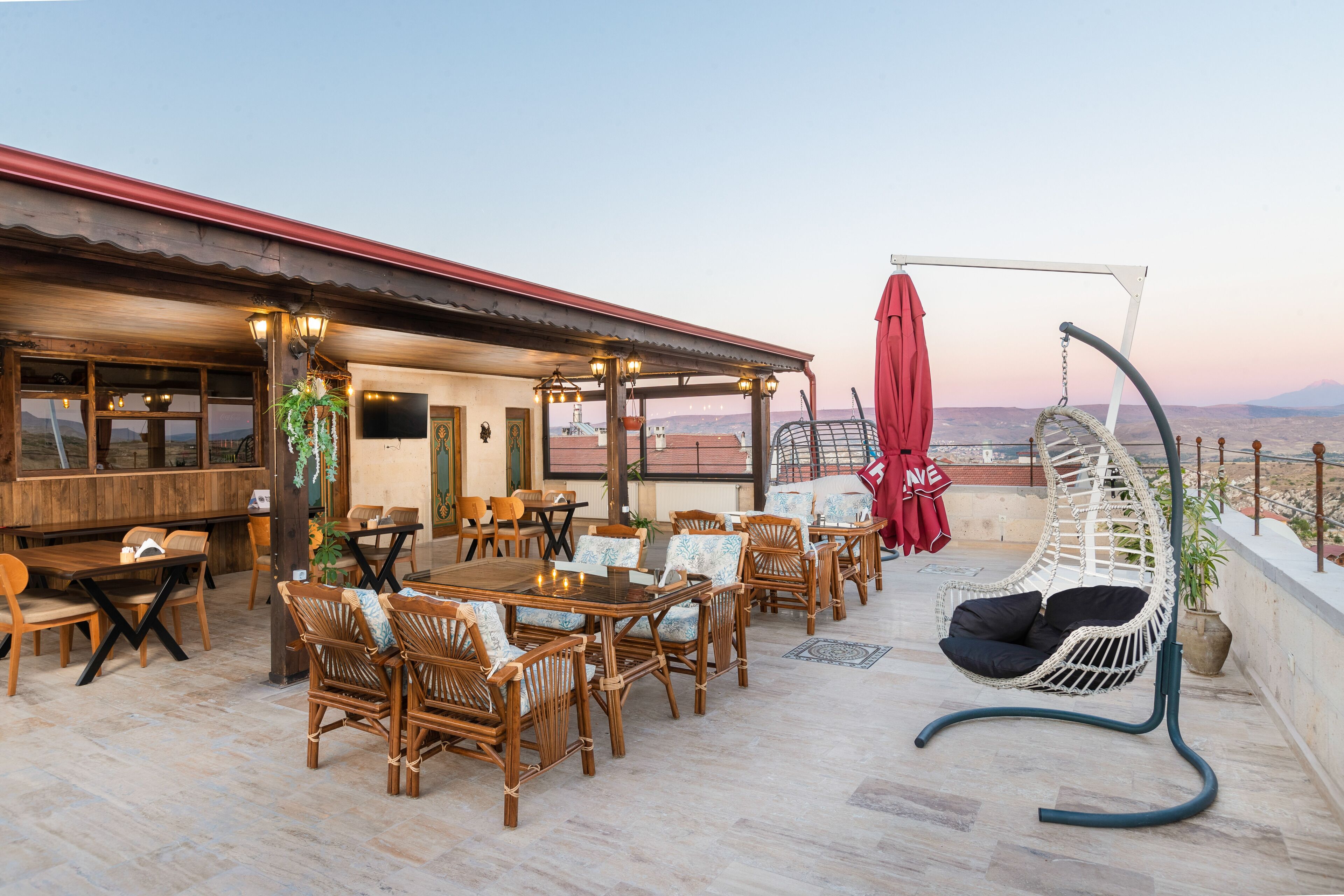 A rooftop terrace with wooden furniture, a hanging chair, and a view of the landscape.