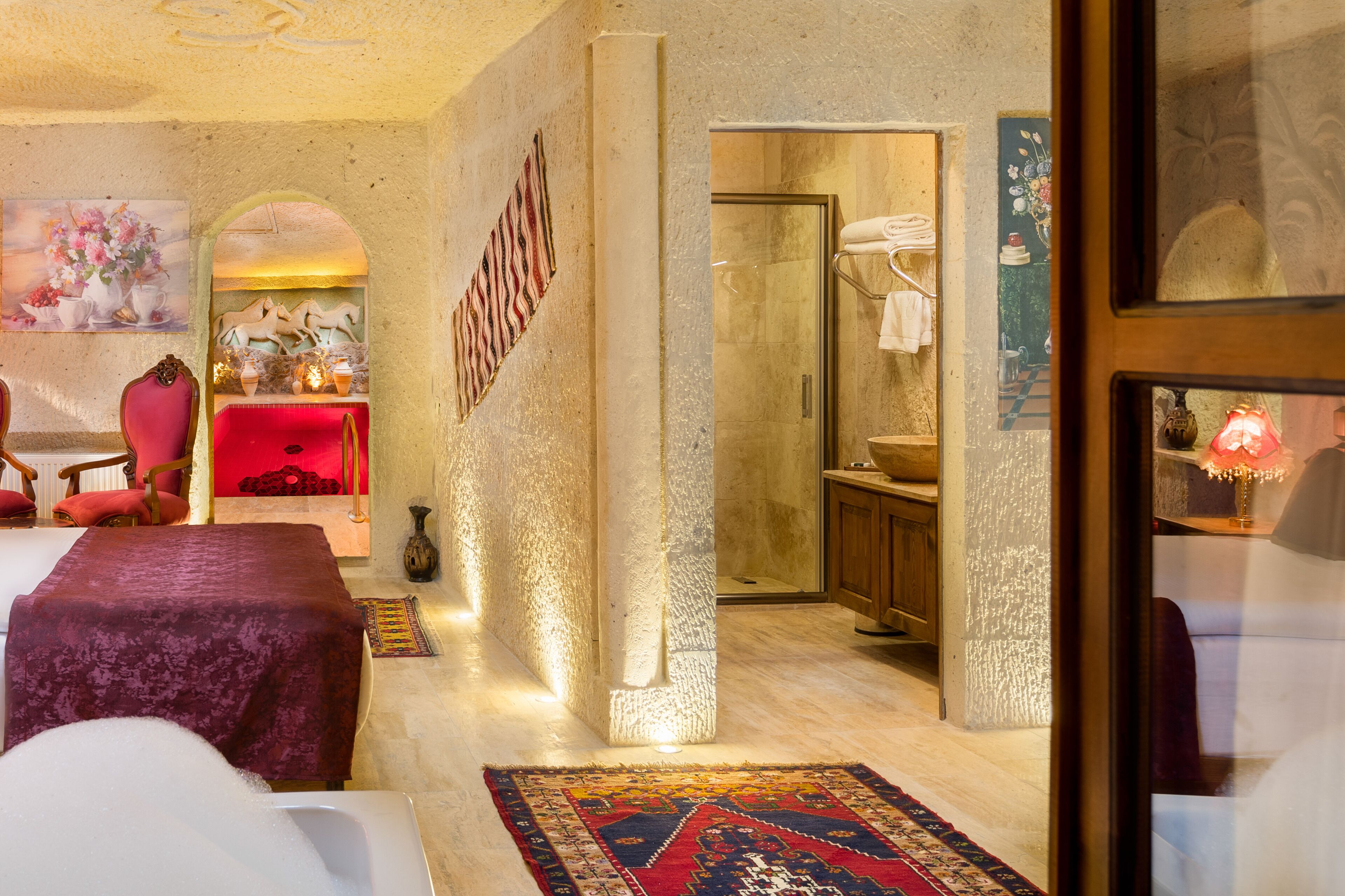 Ein Hotelzimmer mit einem großen Bett, einer Sitzecke mit einem roten Sessel, einem kleinen Tisch und einem dekorativen Teppich.