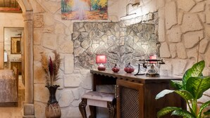 Un mur de pierres, un banc en bois rustique et une table avec une lampe et des objets décoratifs.