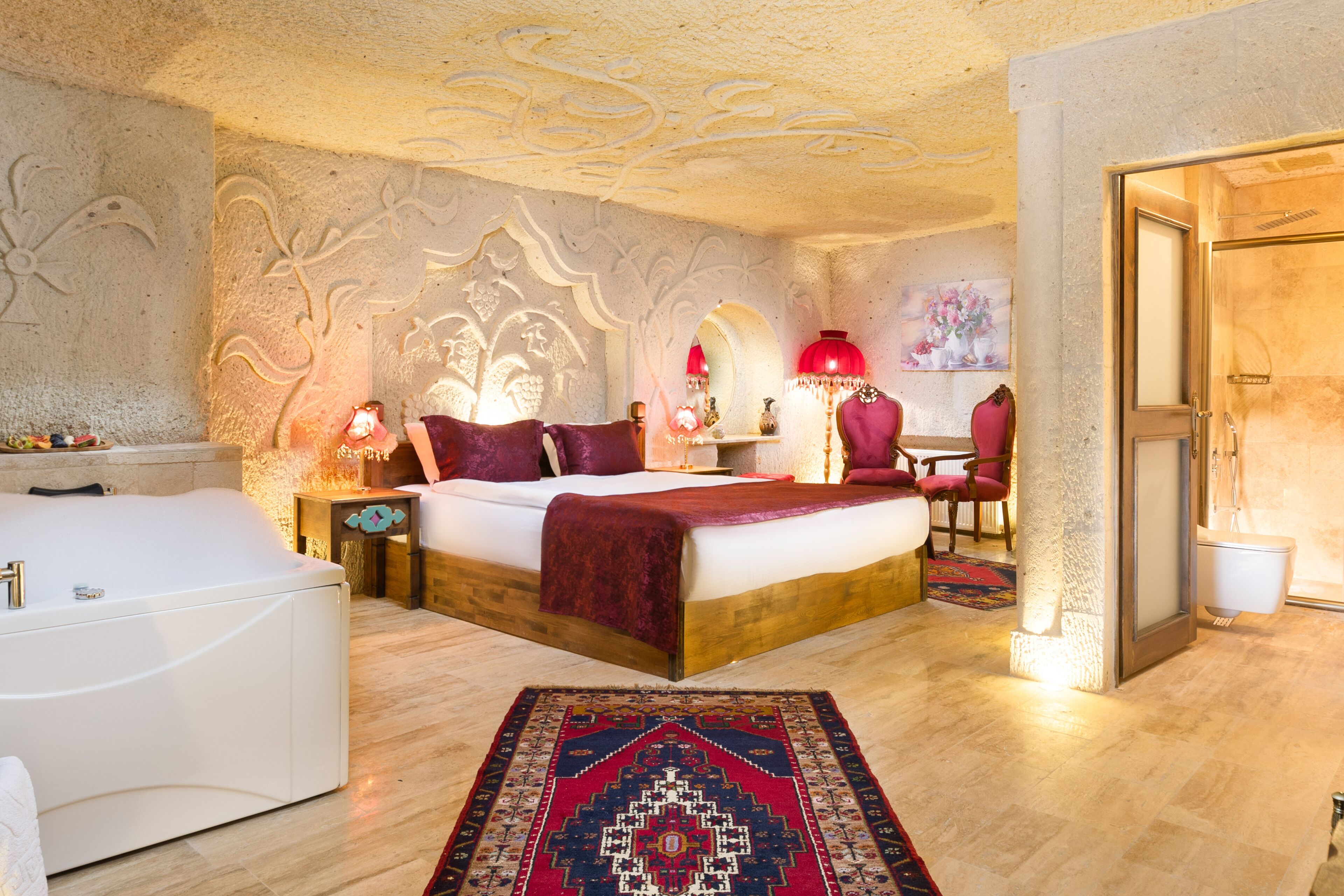 Een slaapkamer met een groot bed, een zithoek met een stoel, een klein tafeltje en een decoratief vloerkleed.