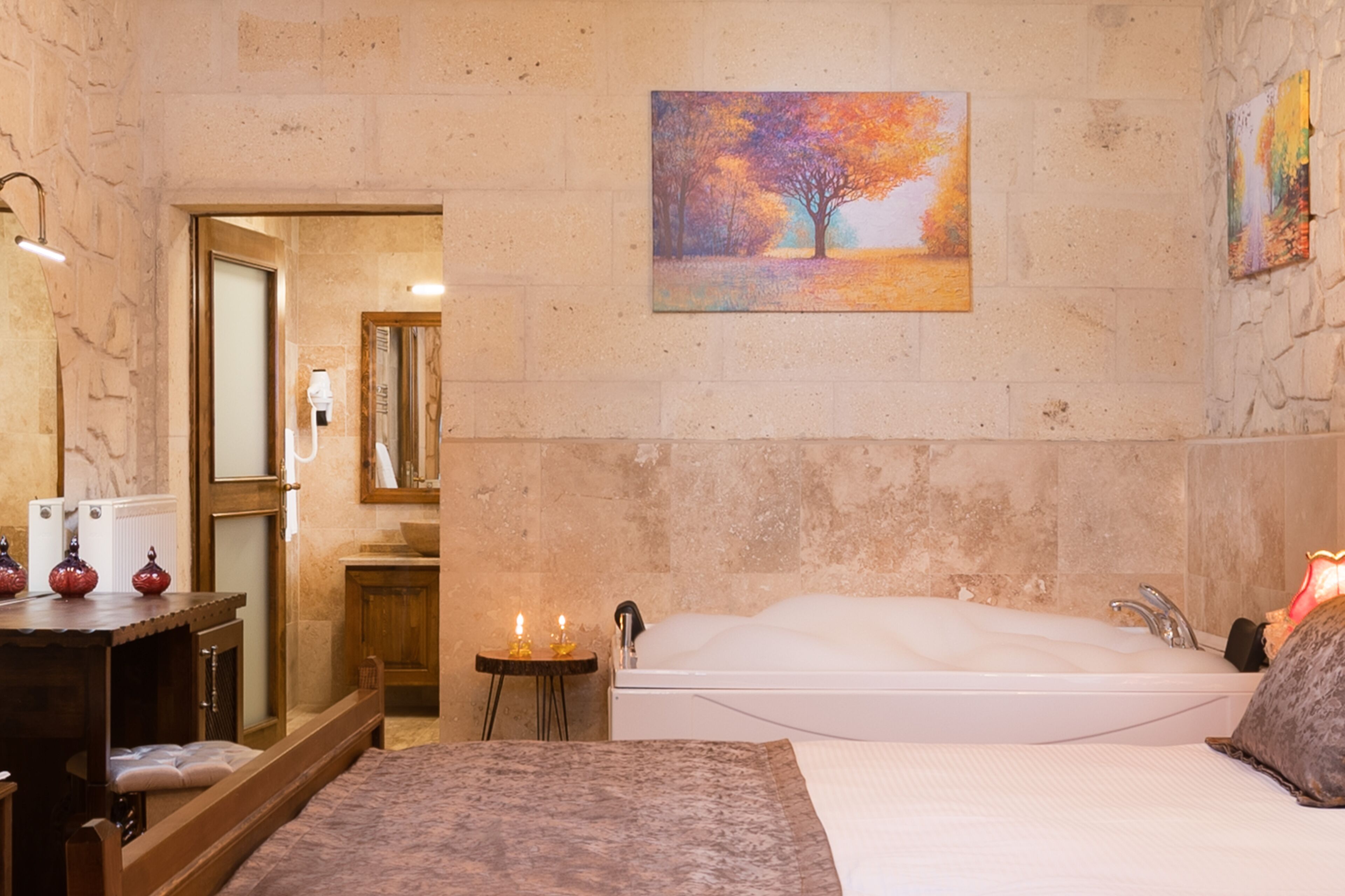 A room with a large bed, a bathtub, a wooden dresser, and a painting of a tree on the wall.