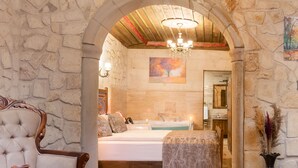 Une chambre aux murs de pierre, avec un grand lit, une chaise en bois, une coiffeuse et un lustre.