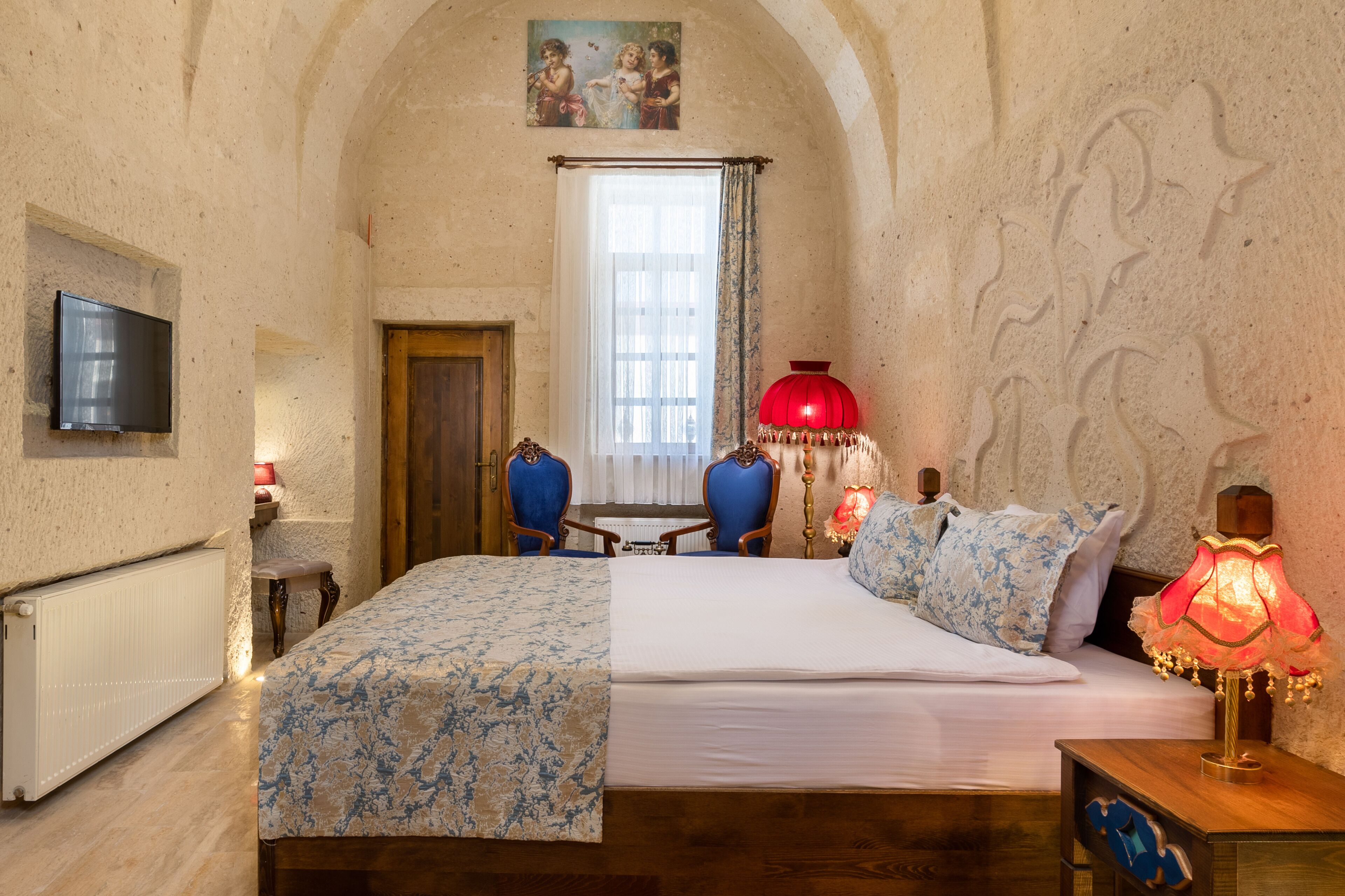 A bedroom with a bed, two chairs, a red lamp, and a painting on the wall.
