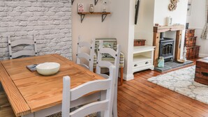 Ein Essbereich mit einem Holztisch und weißen Stühlen, einer Ziegelwand mit dem Schriftzug "ORGANIC", Regalen mit Dekoration und einem Kamin mit Aufbewahrungsboxen.