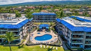 Ein Hotel mit einem zentral gelegenen Schwimmbad, umgeben von Liegebereichen und mehreren Etagen mit blauen Flachdächern.