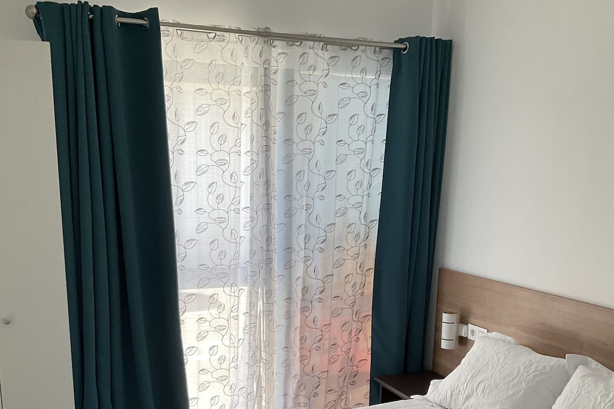 A hotel room with a bed, curtains, a window with a leaf pattern, and a bedside table.