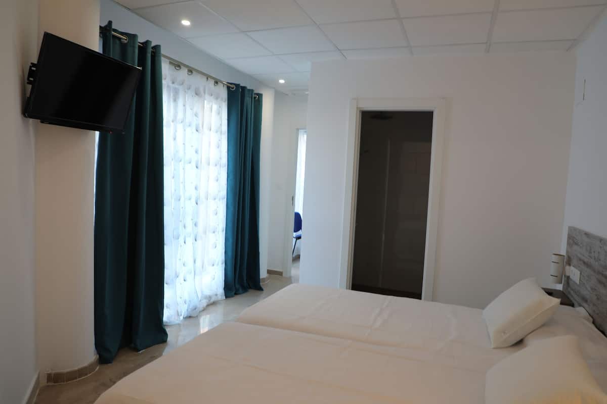 A hotel room with a bed, a flat-screen TV mounted on the wall, and a door leading to another room.