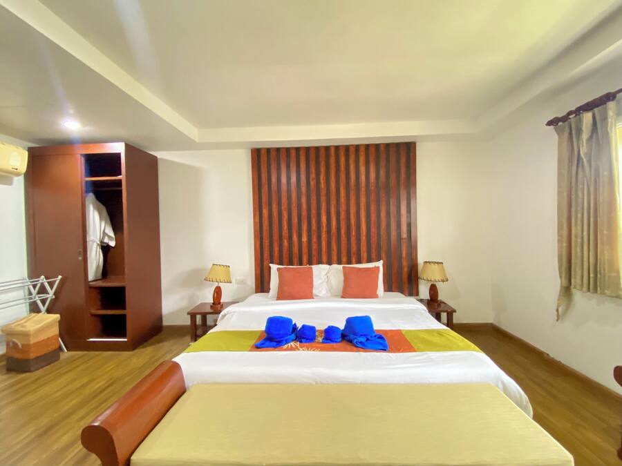 Una habitación de hotel con cama, mesitas de noche, armario y ventana con cortinas.