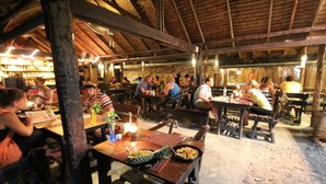 An outdoor restaurant with wooden tables and benches, surrounded by a rustic stone wall.