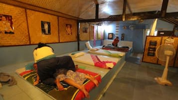 Ein Zimmer mit einem Bett, einem Ventilator und einer Person, die im Bett liegt.