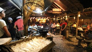 A bustling outdoor dining area with tables and chairs, a large ice-filled container, and a bamboo structure overhead.