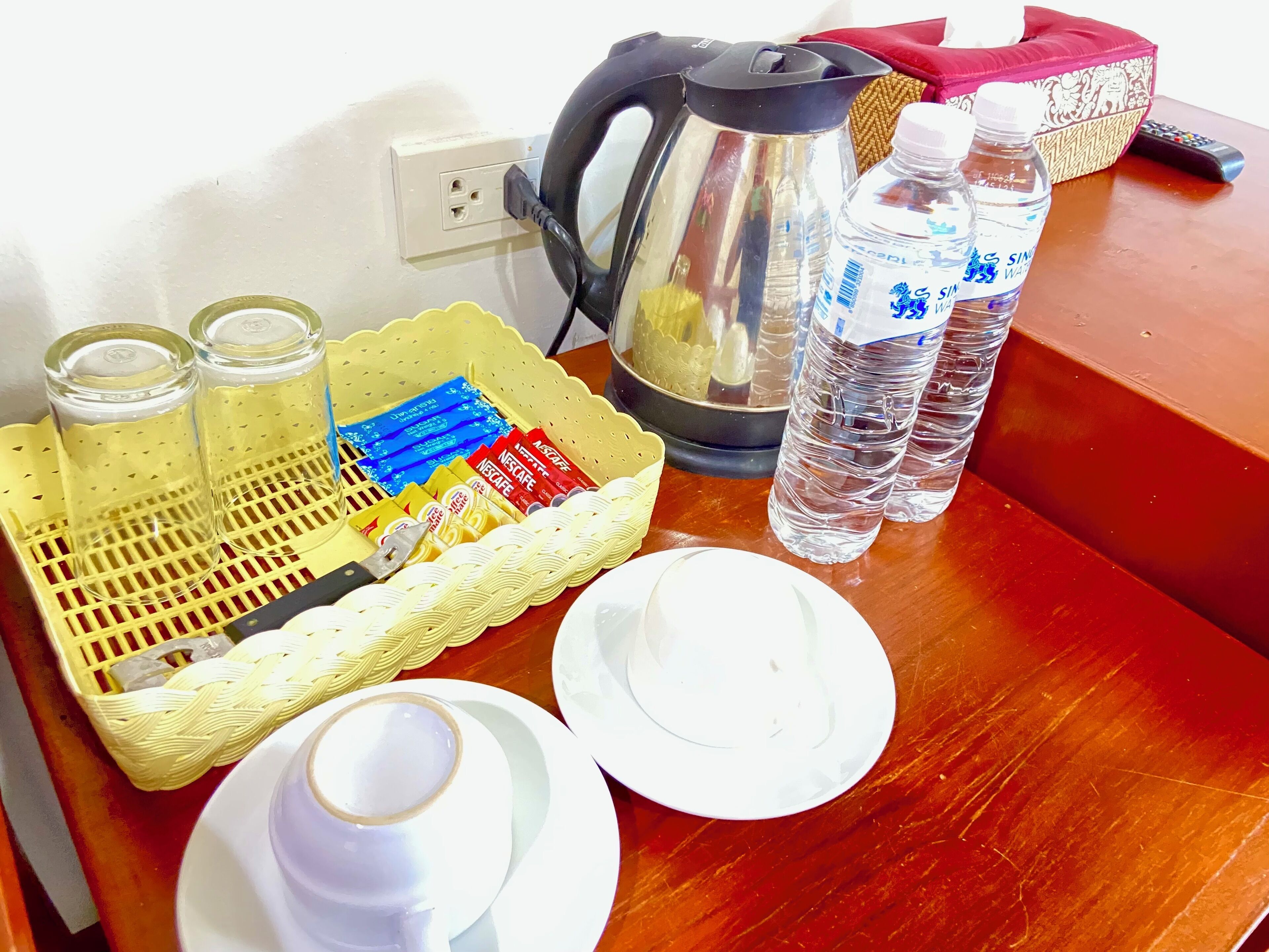 Una bandeja con cafetera, botellas de agua, una cesta de sobres de Nescafé y una taza de café.