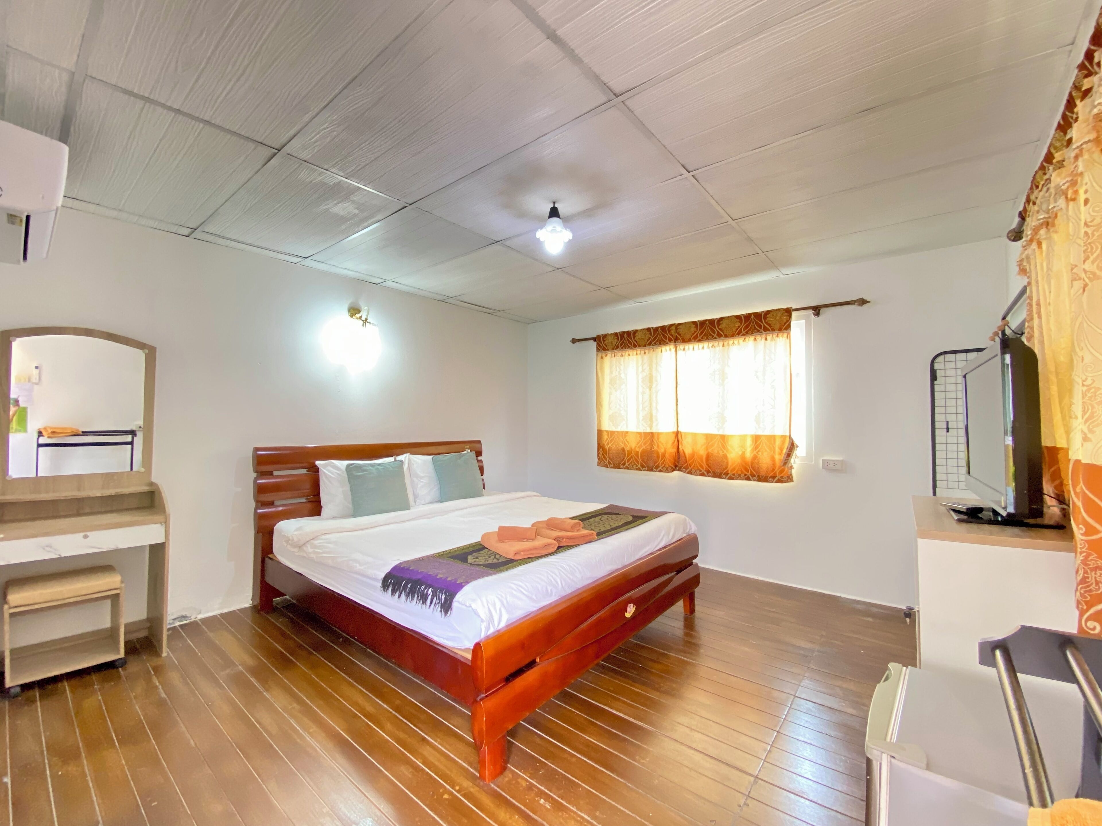 A bedroom with a wooden bed, a bedside table, a mirror, a window with curtains, and a ceiling fan.