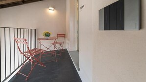 Un balcon avec une table et des chaises, une petite plante en pot et une œuvre d’art accrochée au mur.