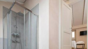 Une salle de bain moderne avec une douche à parois de verre, un lavabo et des toilettes. Des marches mènent à une porte qui donne sur un espace de vie équipé d’un téléviseur à écran plat.
