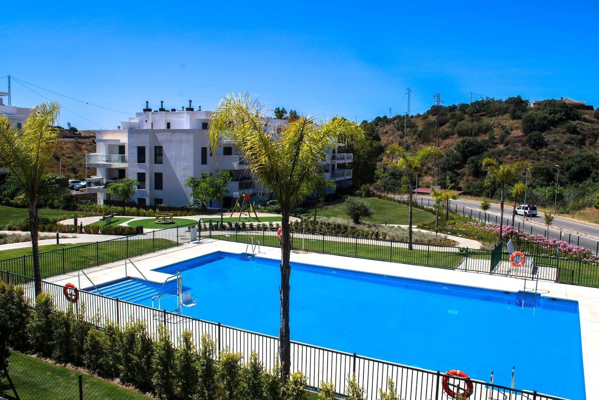 A swimming pool with a lifebuoy, surrounded by a fence and greenery, with a building in the background.