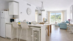Una cocina moderna con comedor, armarios blancos, un reloj y vistas a zonas verdes.