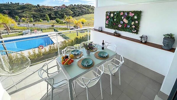 Un balcón con una mesa de comedor preparada para cuatro personas, con vista a una piscina y un paisaje pintoresco de colinas.