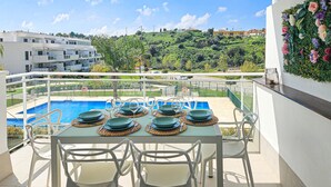 Terraza en la azotea con piscina, mesa de comedor dispuesta con platos y vasos, sillas blancas y un muro decorativo.