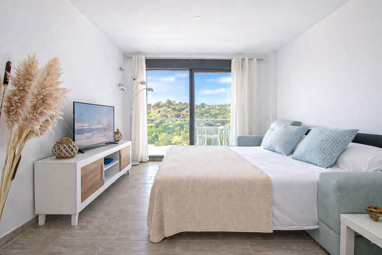 Een slaapkamer met een bed, een televisie, uitzicht op groen en een balkon.