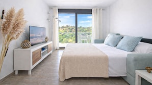 Un dormitorio con cama, televisión, vista a follaje y balcón.
