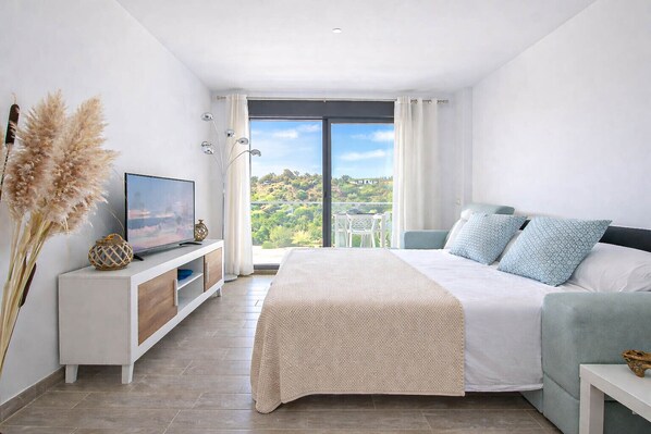 Un dormitorio con cama, televisión, vista a follaje y balcón.