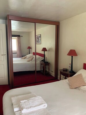 Ample storage space is provided by the large mirror wardrobe with a sliding door. The room features a single bed with bedside tables and a small table.