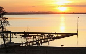 Un coucher de soleil sur un lac paisible, avec une jetée en bois qui s’avance dans l’eau.