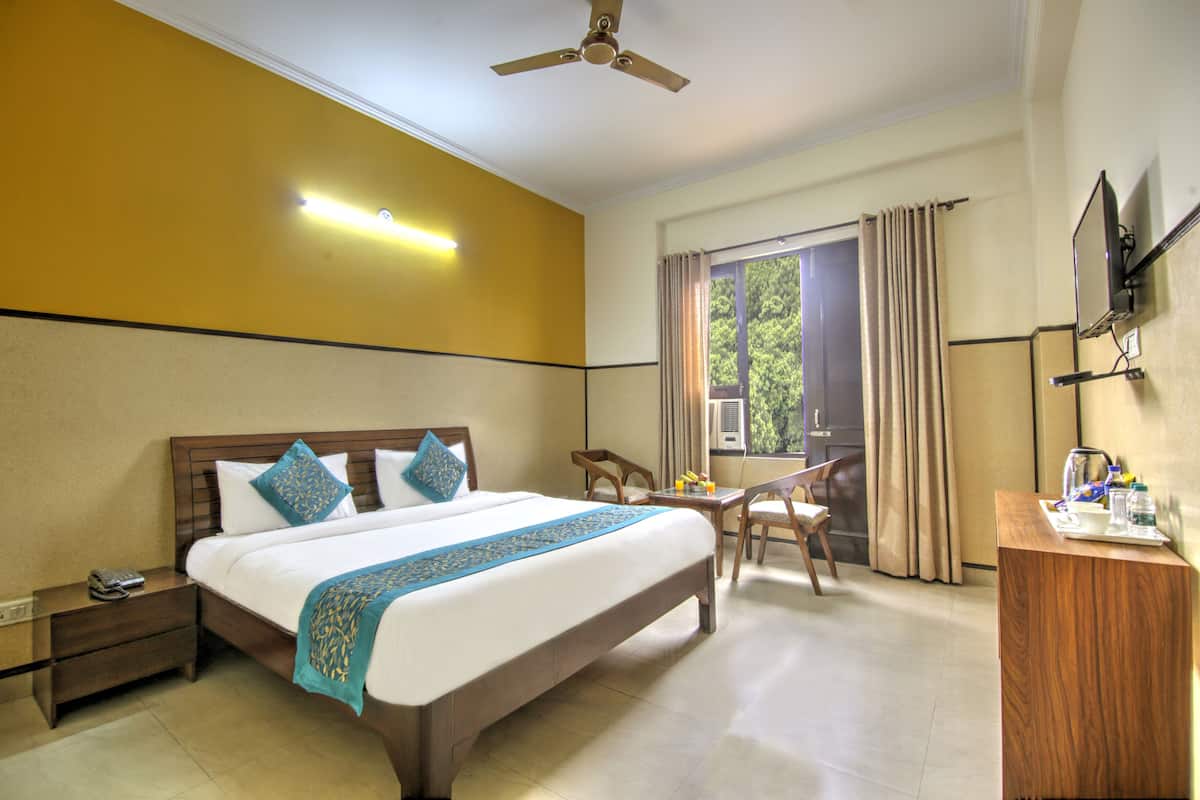 A hotel room with a bed, bedside table, desk, chair, and a TV on the wall.