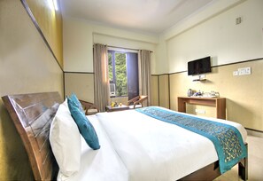 Una habitación de hotel con cama, televisor, escritorio y ventana con cortinas.
