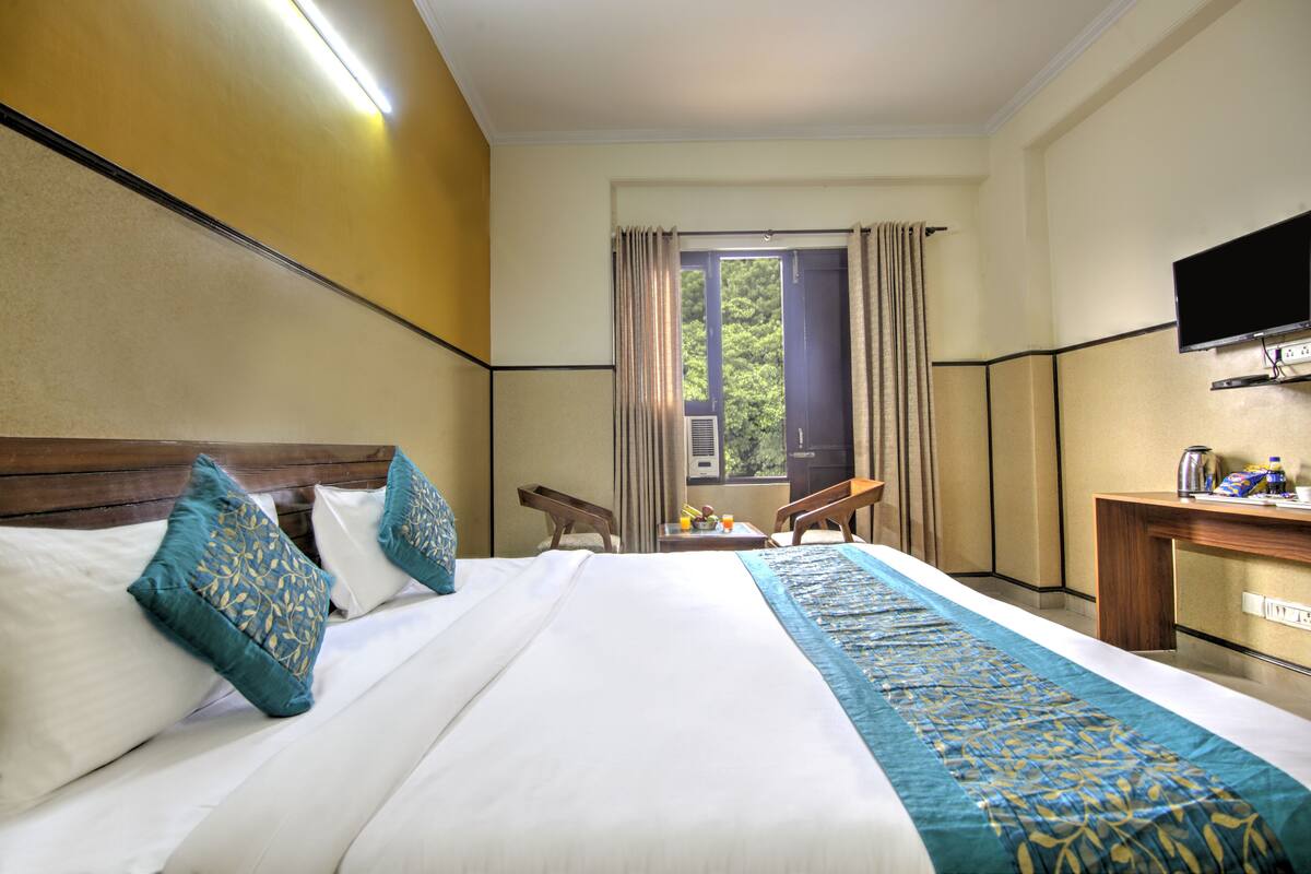 A hotel room with a large bed, a desk, a chair, a television, and a window with curtains.