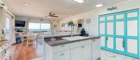 A spacious kitchen with a large island, white cabinets, and a teal door.